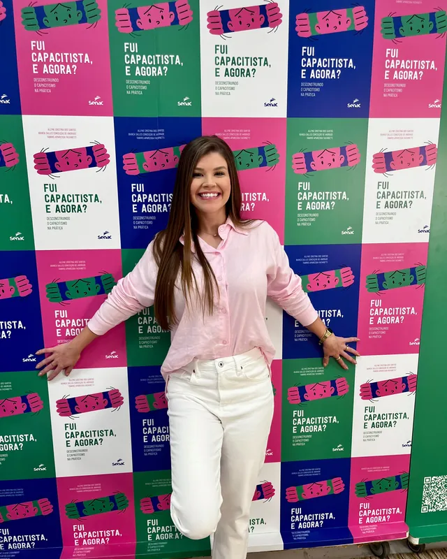 Bianca Salles em frente ao painel do lançamento, coberto por repetições da capa de Fui capacitista, e agora?