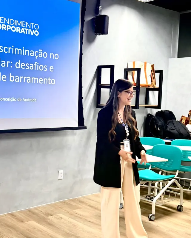 Bianca Salles gesticulando durante uma formação, ao lado do slide “Preconceito e discriminação no ambiente escolar”.